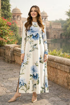 Woman wearing a floral dress standing in an outdoor setting with architectural elements and greenery.